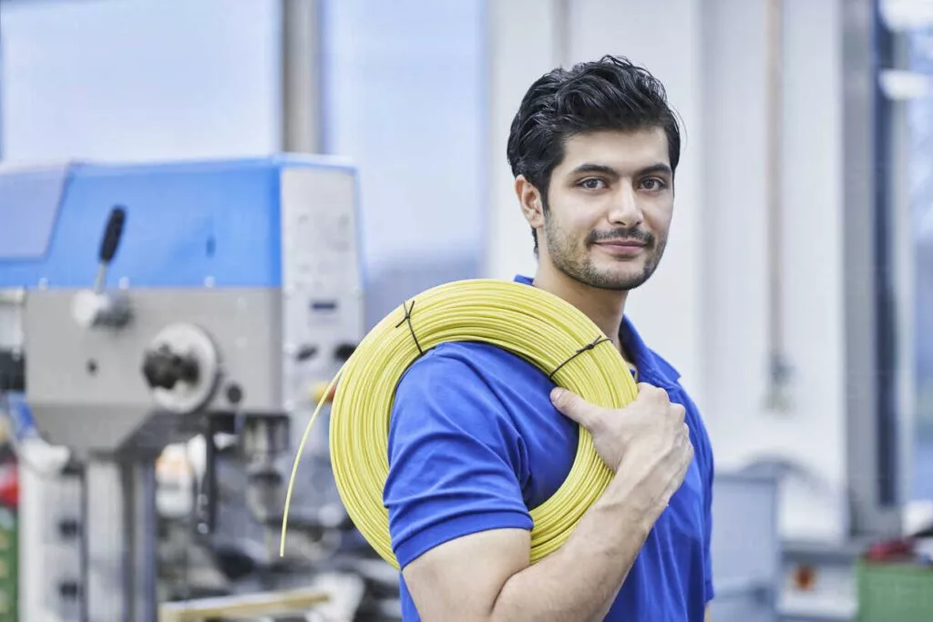 Junger Mann mit Kabelrolle vor einem Fabrikgebäude