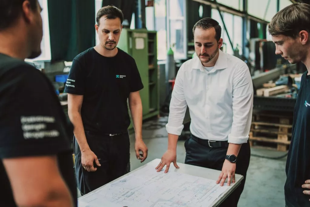 Arbeits-Team in der Fertigung vor einer maschinellen Zeichnung